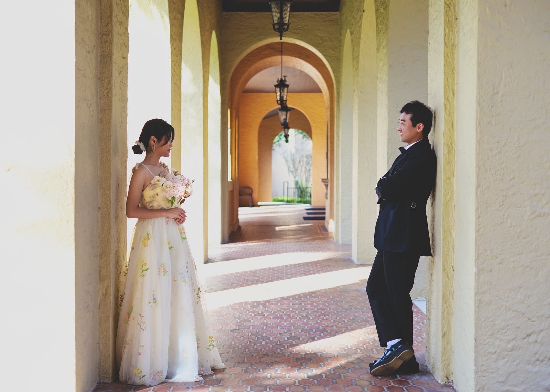 A couple standing across from each other beneath a sunlit arcade