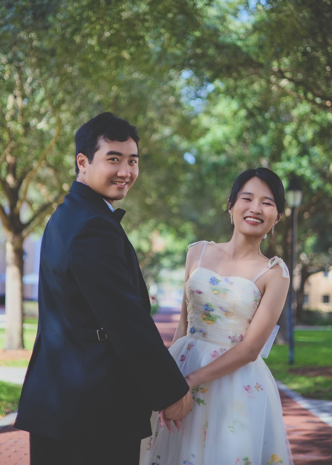 Couple smiling hand in hand on a shaded brick walkway