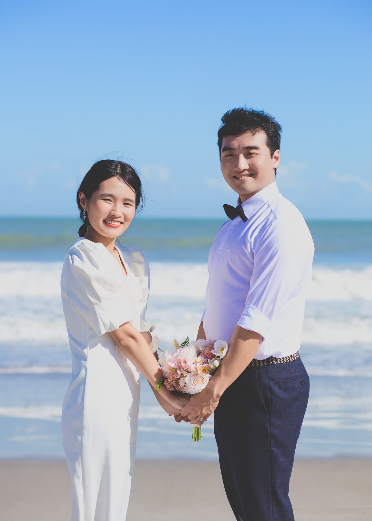 Couple holding a bouquet together at the water's edge