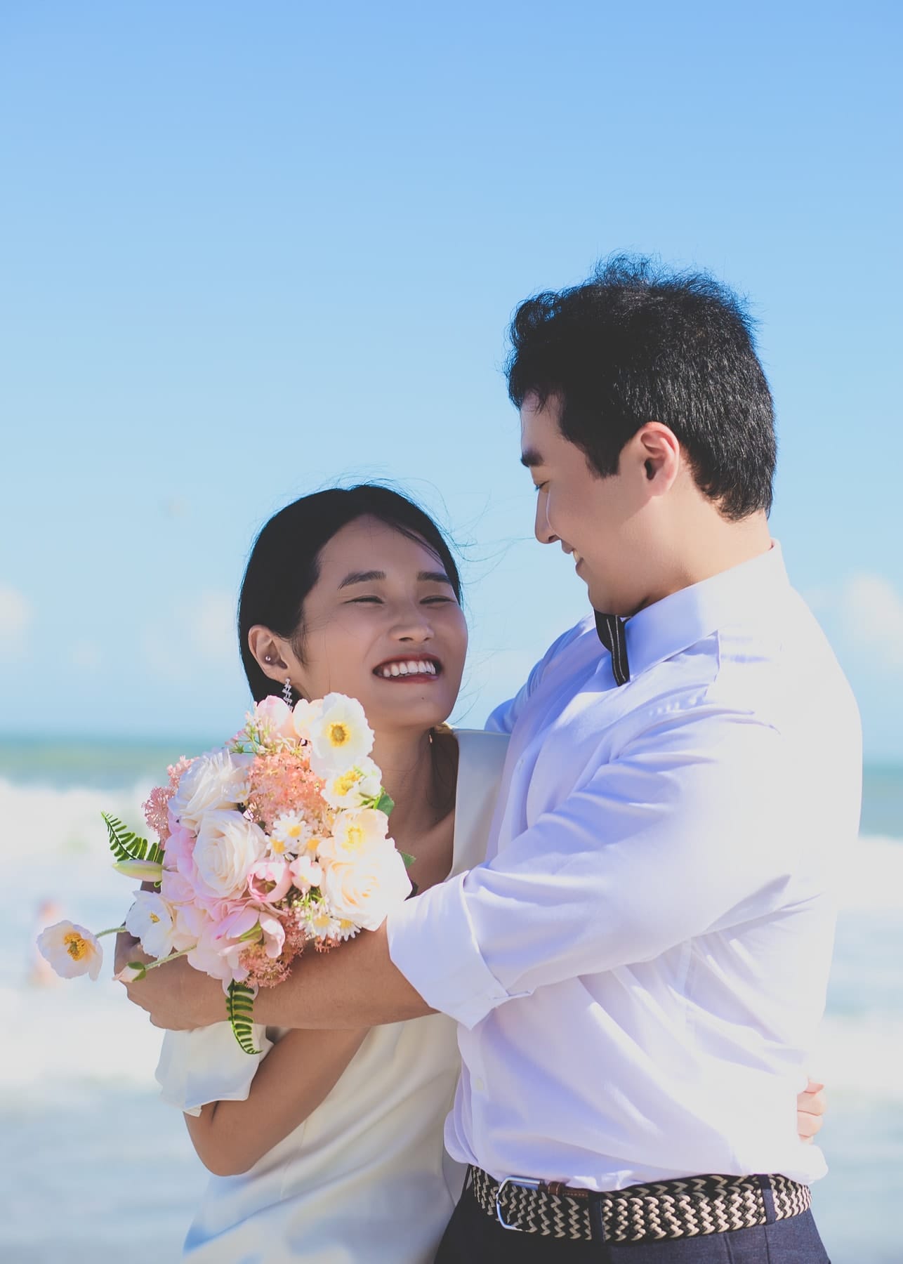 Groom hugging the laughing bride from behind on the beach