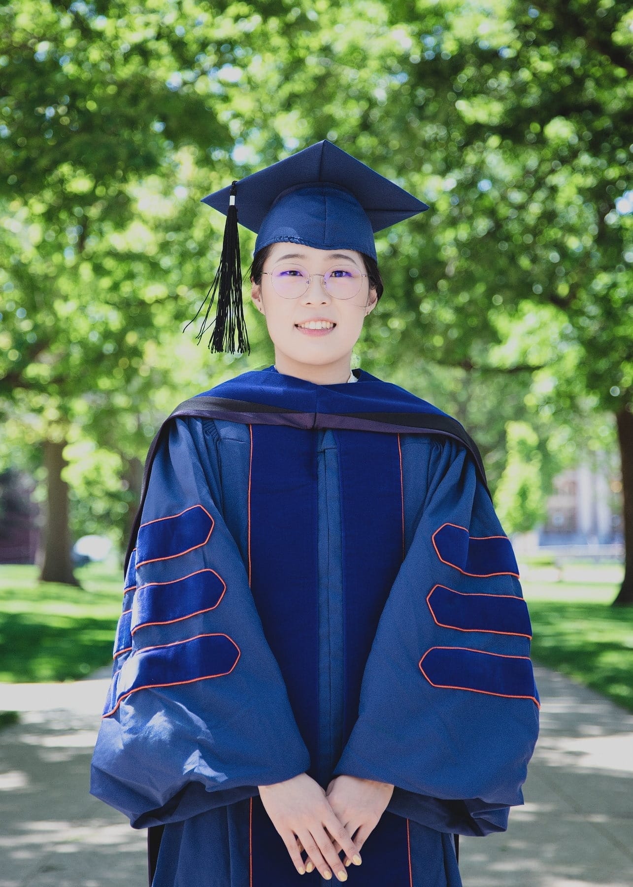 Graduate in academic regalia beneath leafy trees