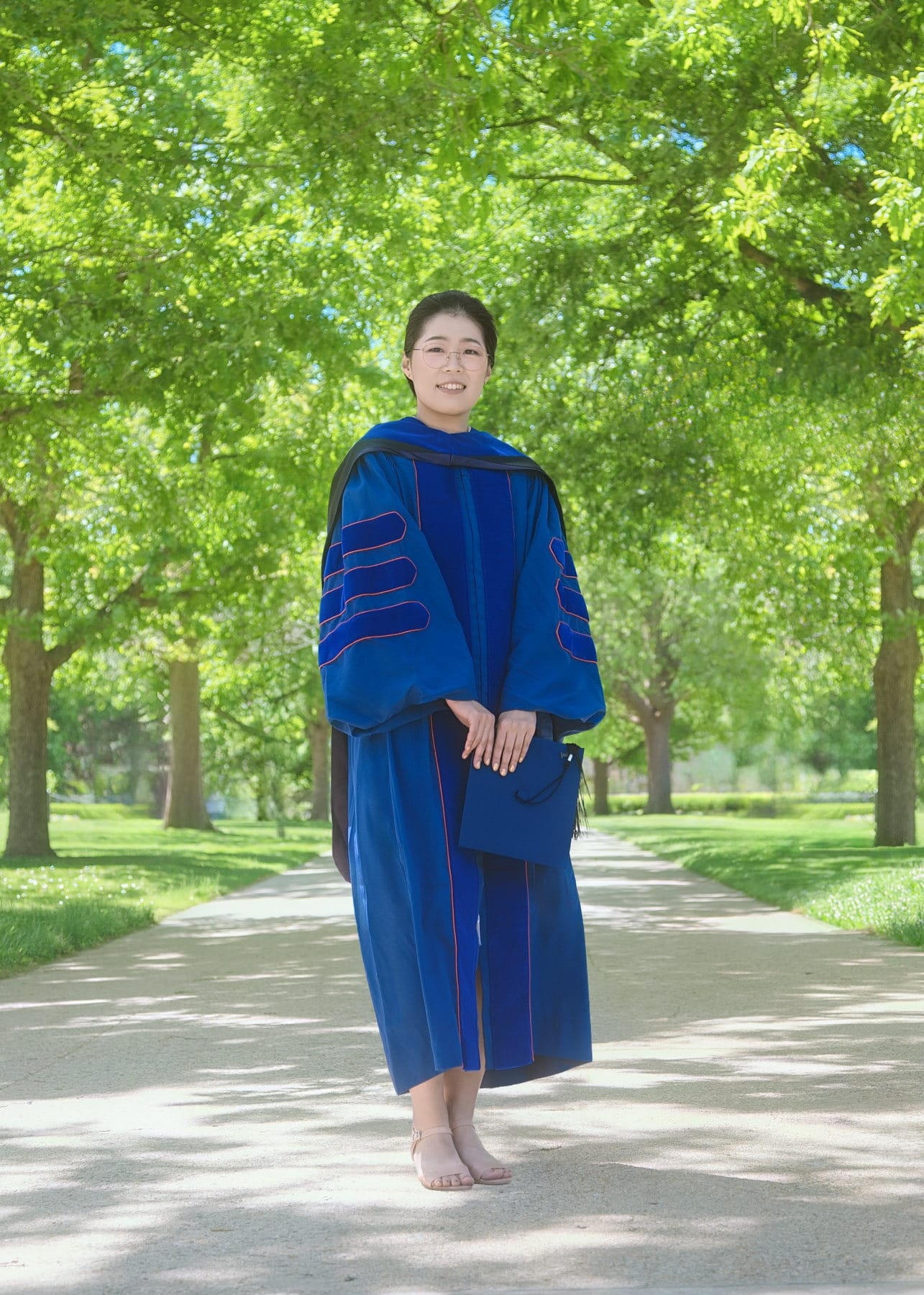 Full-length graduation portrait beneath an avenue of trees