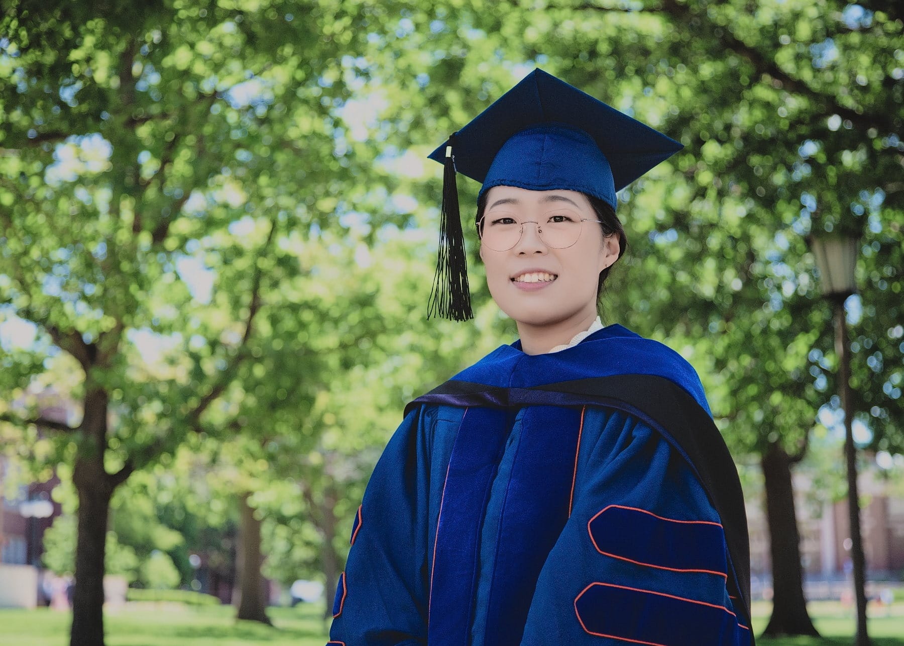 Graduate portrait beneath a broad green tree canopy