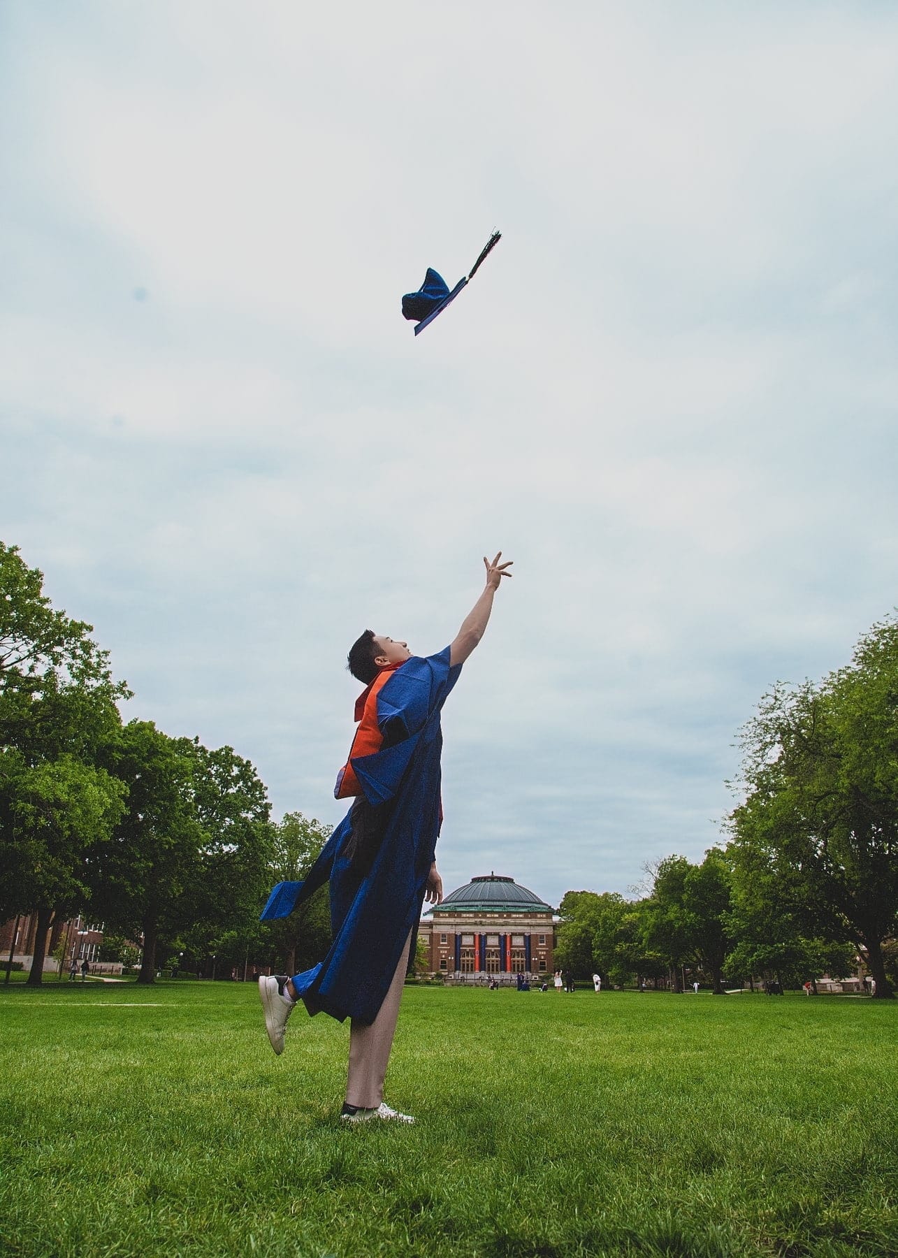 Graduate tossing a cap high above a campus lawn