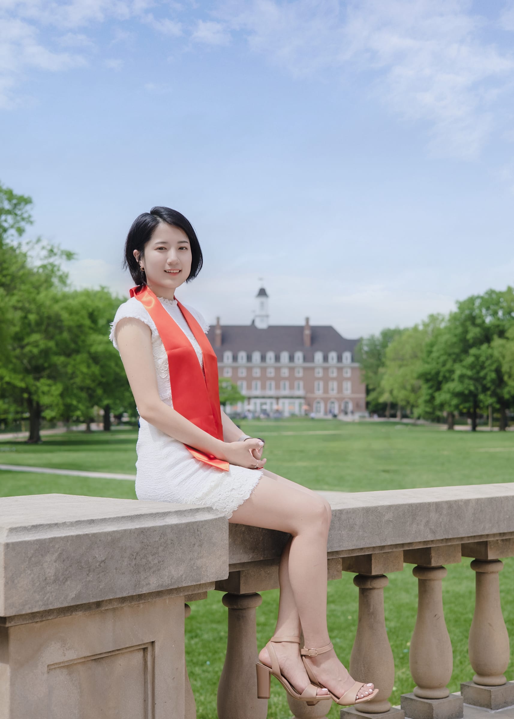 Graduate seated on a stone balustrade overlooking the campus lawn