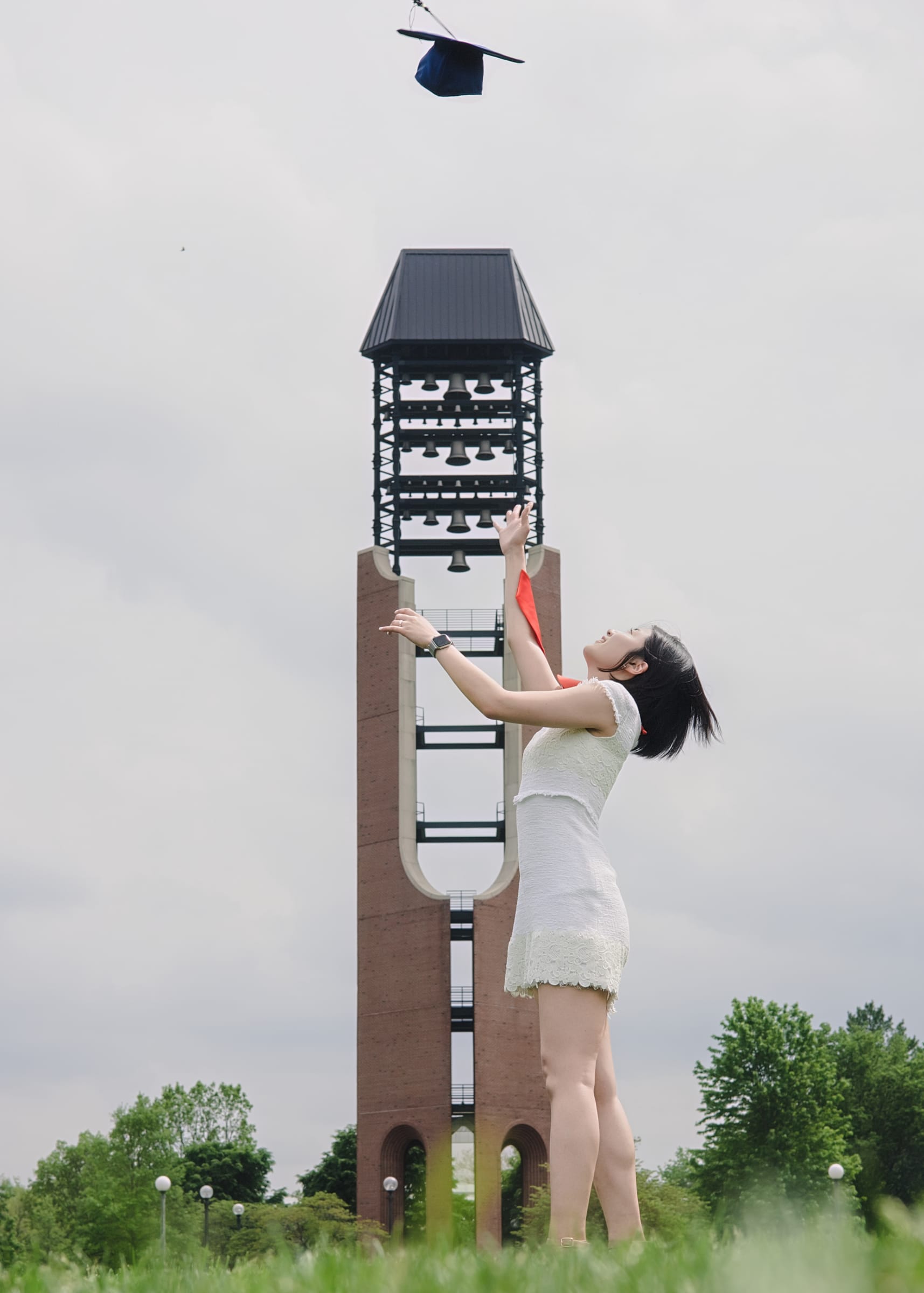Graduate tossing a cap beside a campus bell tower