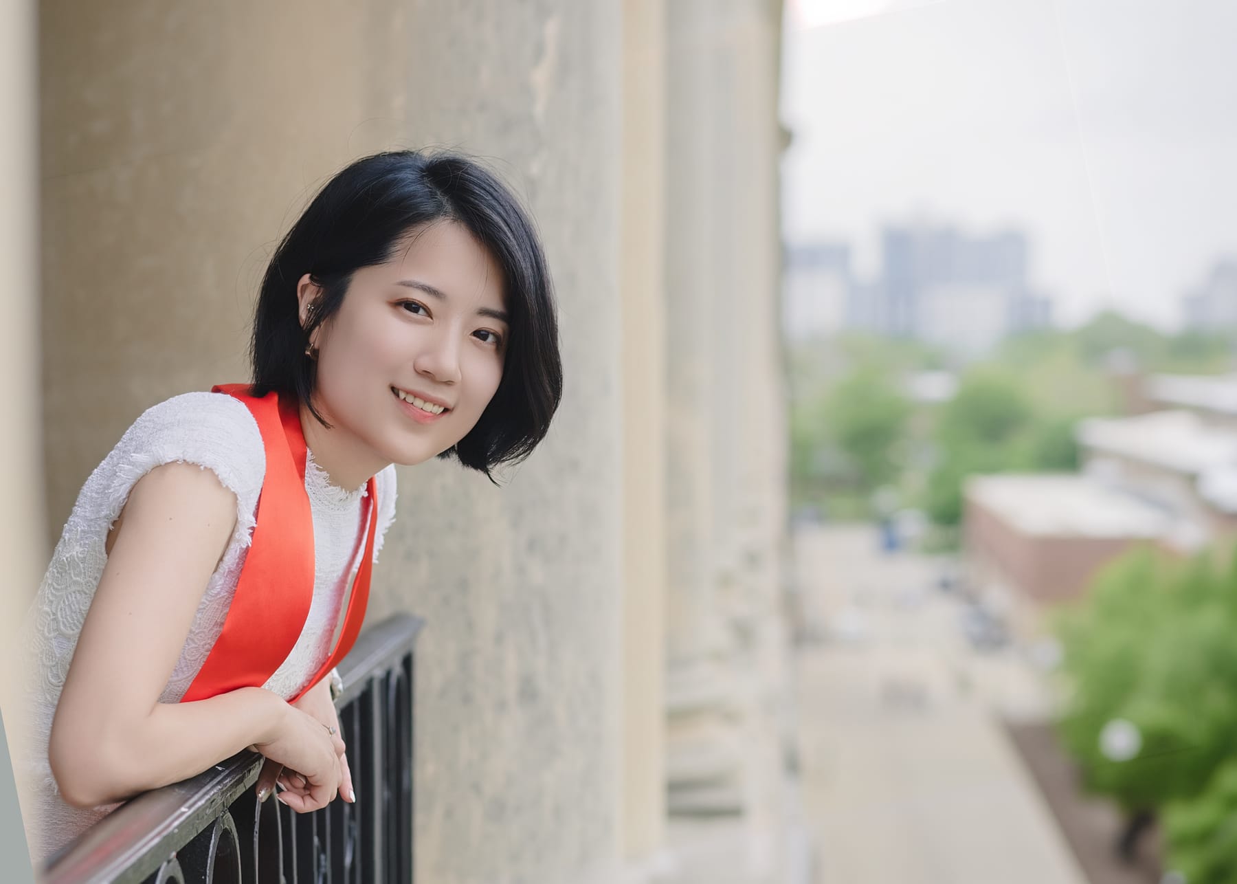 Graduate smiling beside a balcony railing and stone columns