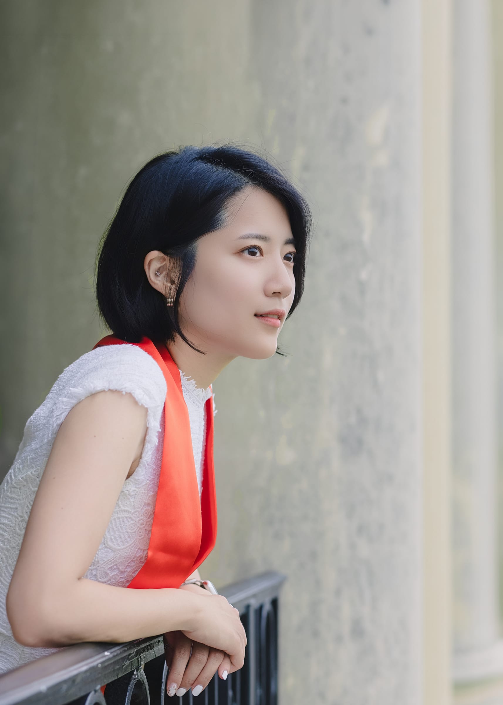 Graduate leaning on a balcony railing beside a stone column