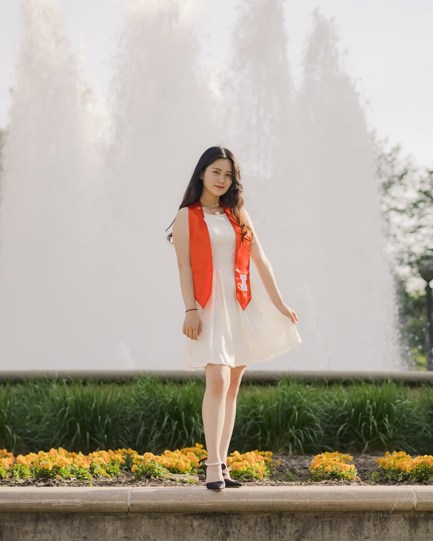 Graduate in a white dress before a campus fountain