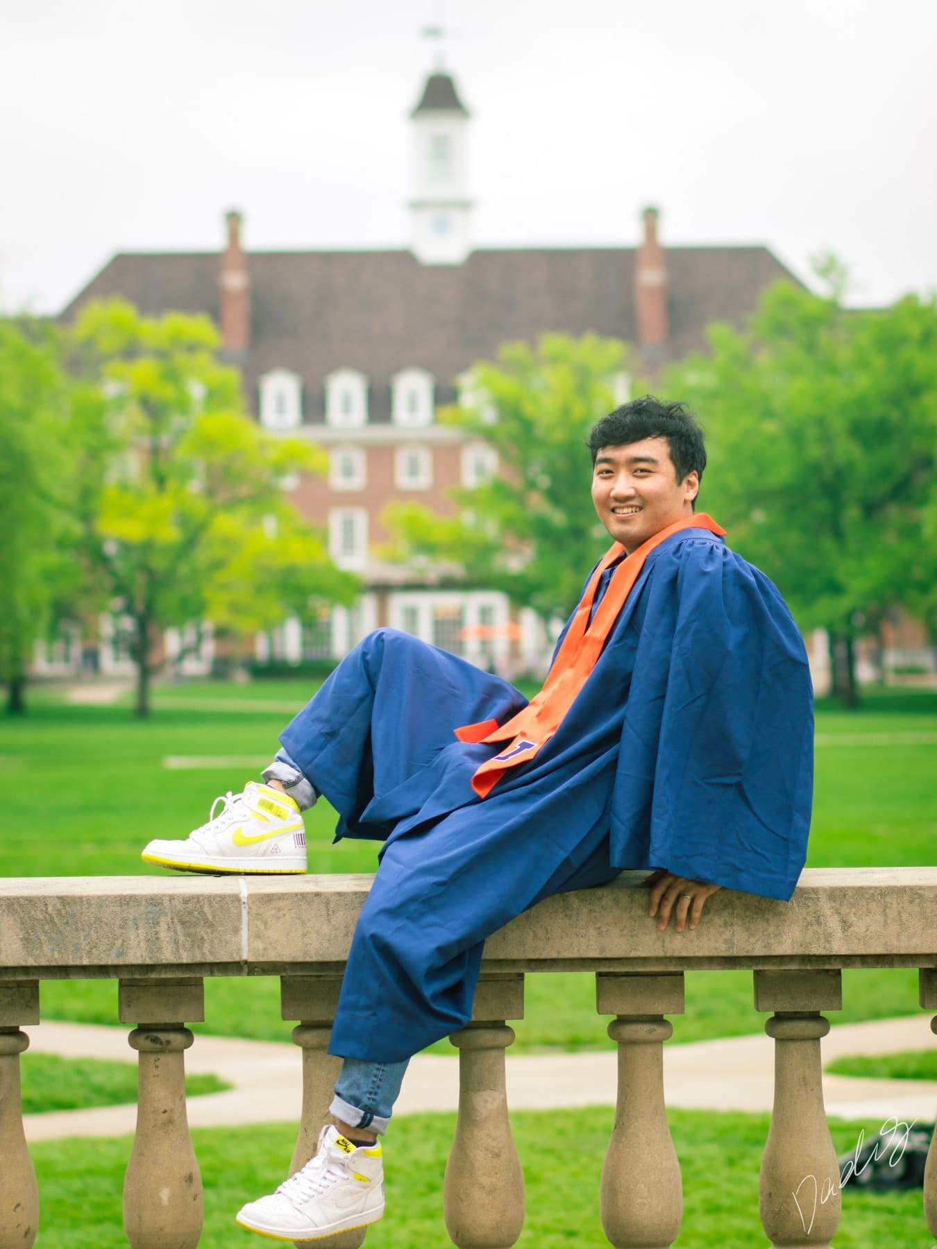 Graduate seated on a stone balustrade before a brick hall
