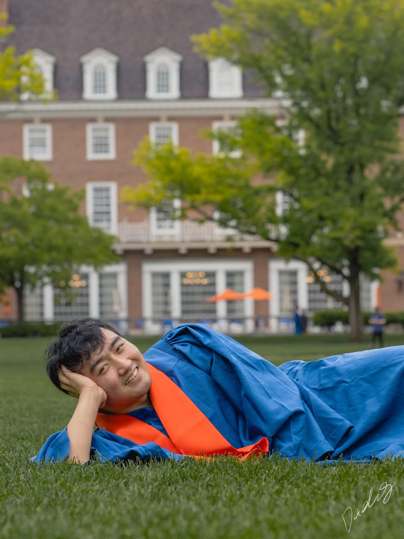 Graduate resting his head on his hand on the grass