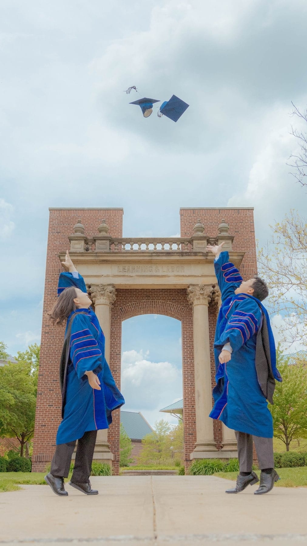 Two graduates throwing their caps beneath a campus arch
