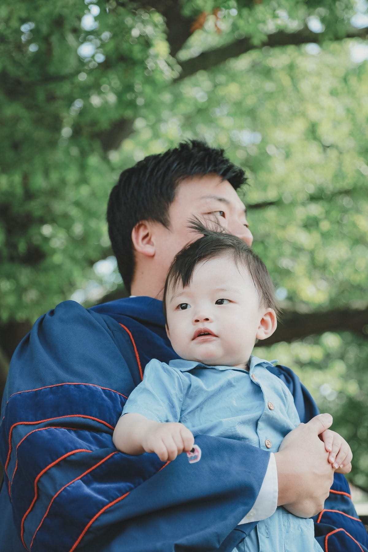Graduate holding a young child beneath trees