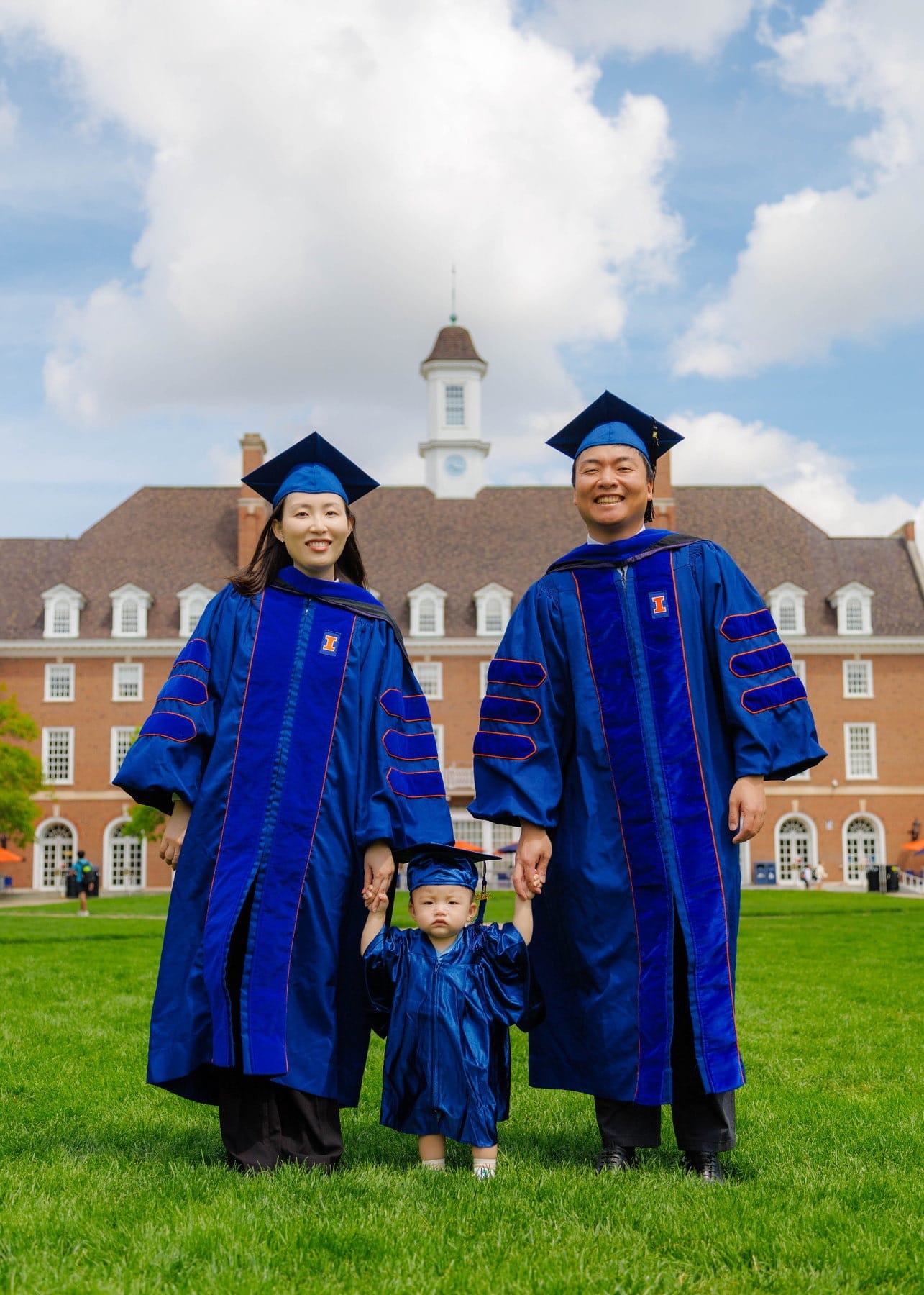 Graduating parents standing with their child on a campus lawn