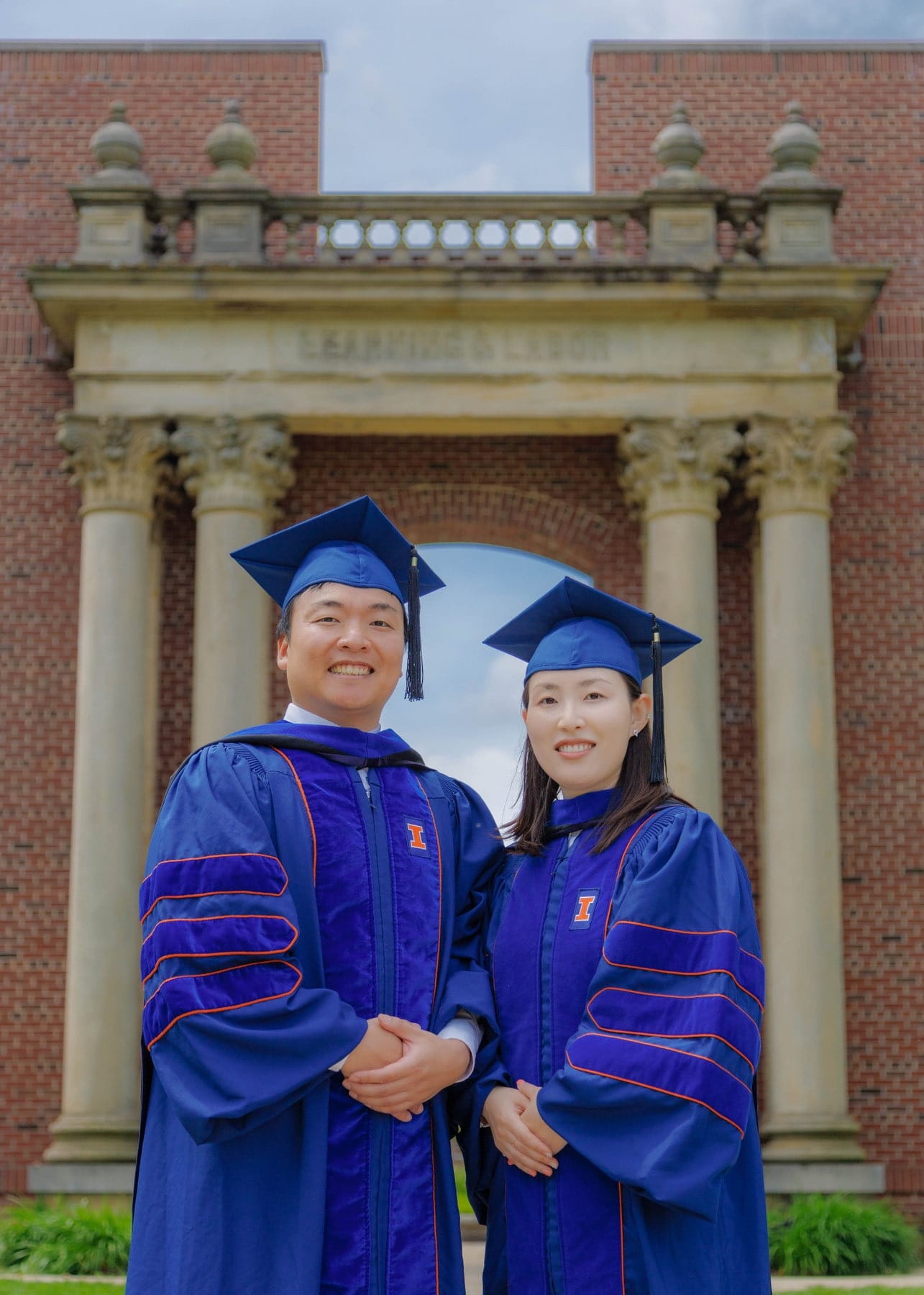 Two graduates posing together in front of a campus arch