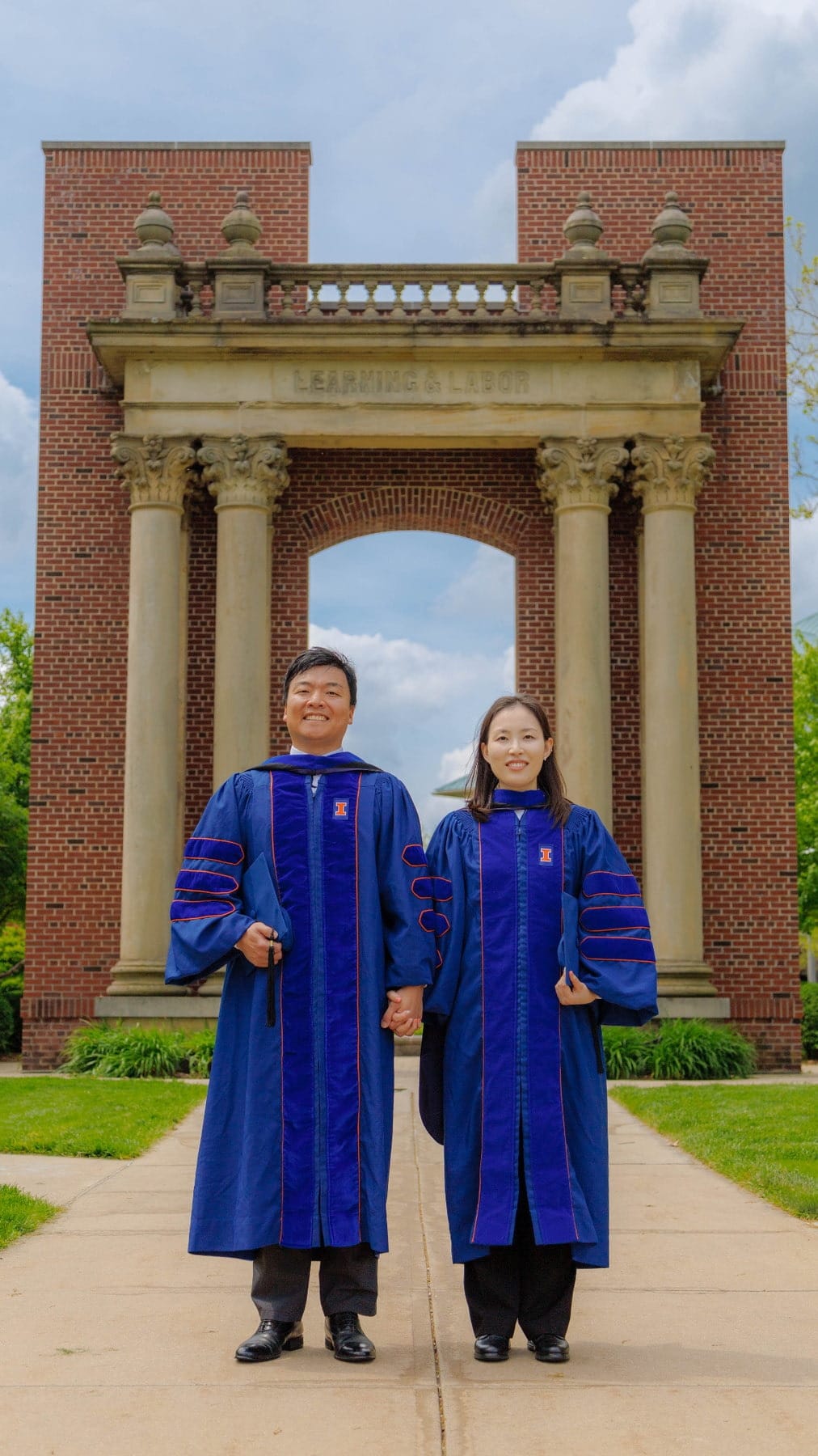Two graduates standing together beneath monumental campus architecture