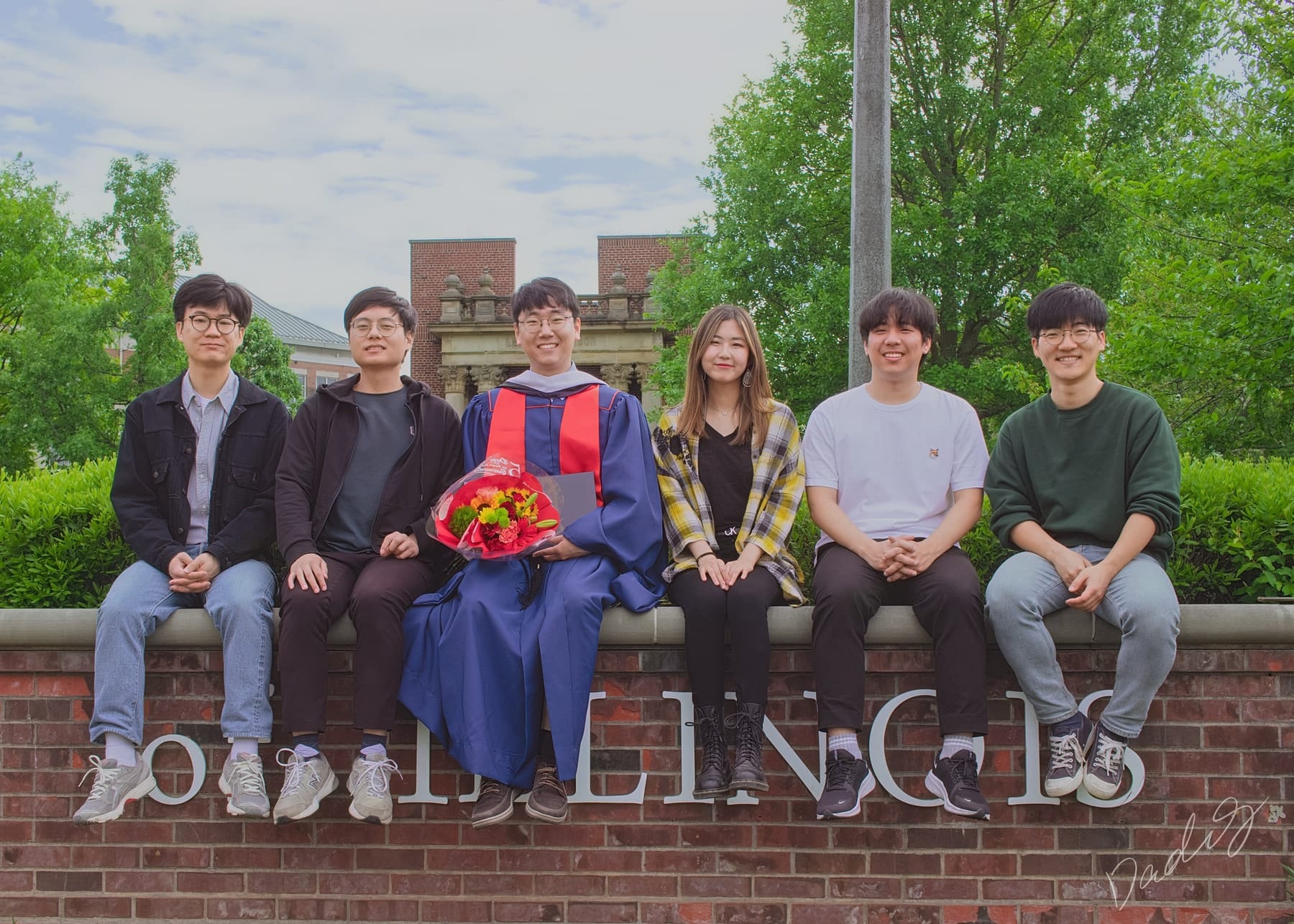 Friends seated along a campus sign with the graduate
