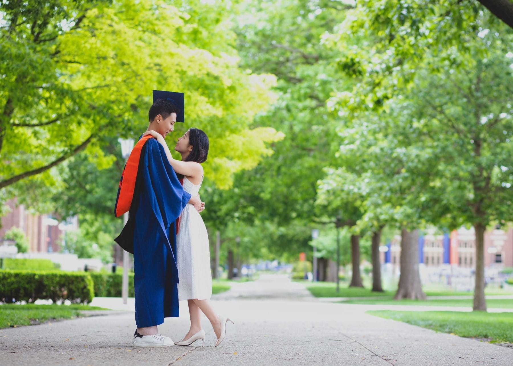 Graduation couple standing together on a leafy campus walkway