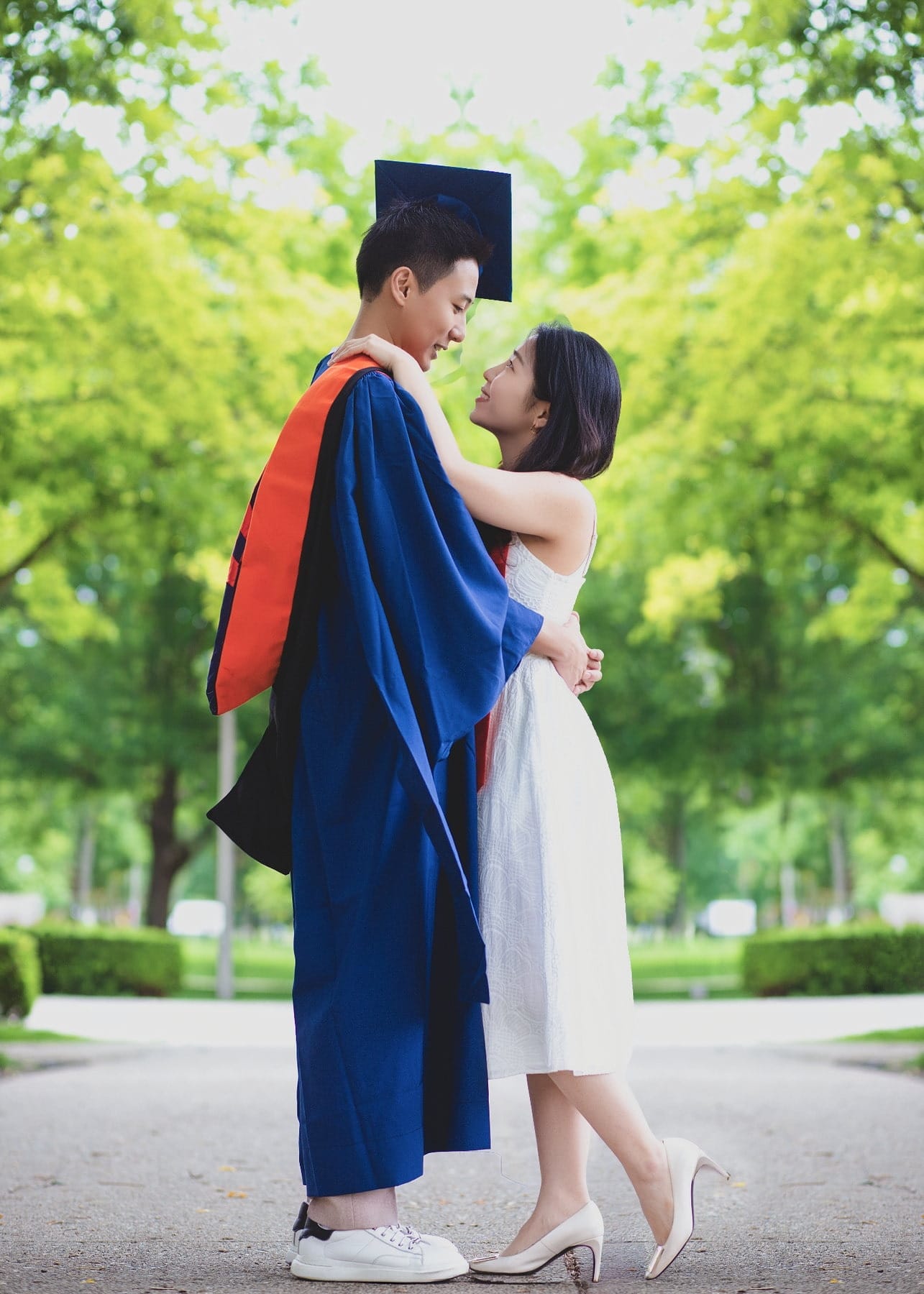 Graduation portrait of a couple embracing beneath green trees