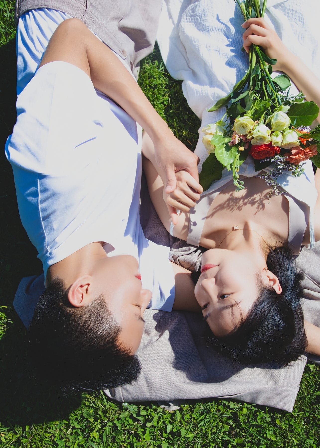 Quiet overhead detail of a couple holding hands beside flowers