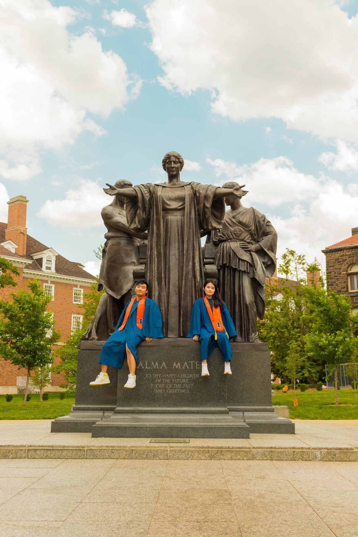 Two graduates seated at the Alma Mater statue