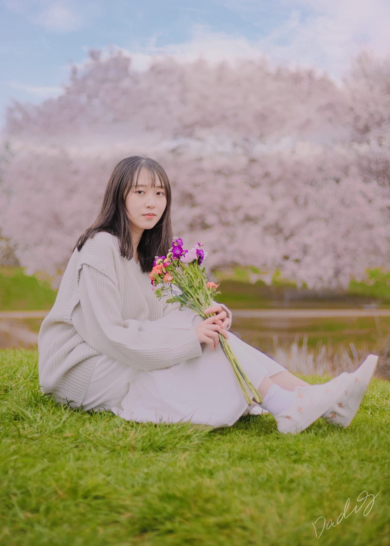 Seated on the grass with a bouquet before blossoming trees