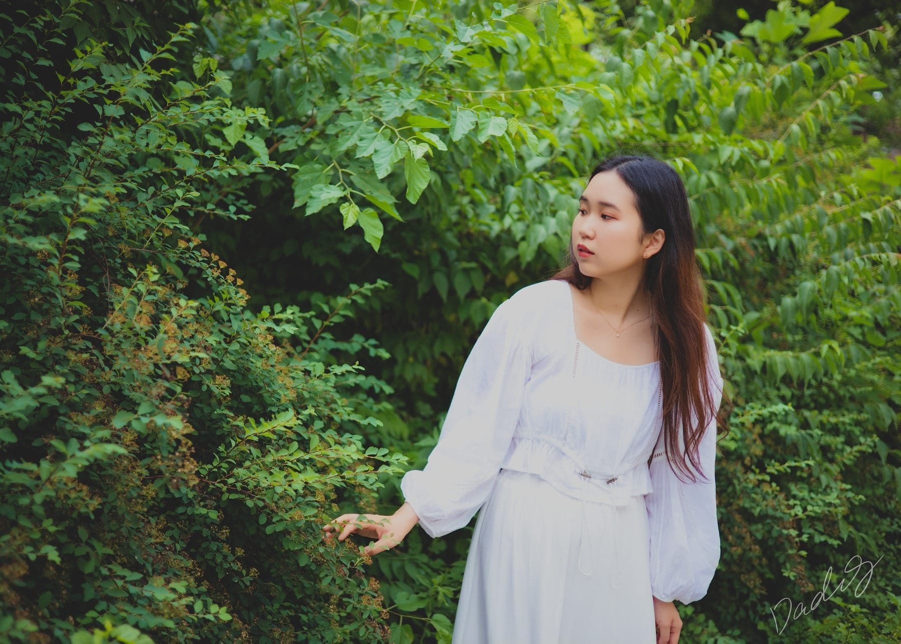 Standing in a white dress before green shrubs